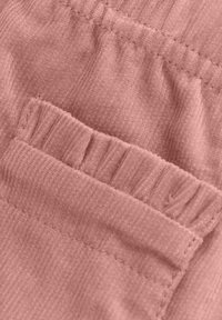 Texturerad rosa tyg med vertikal ribbning har ett gathers elastiskt midjeband och en liten ficka med en volangkant.
