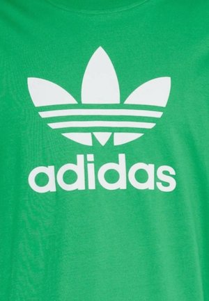 T-shirt verde in cotone con logo Adidas bianco, caratterizzato da tre foglie stilizzate e tre strisce orizzontali sotto il testo.