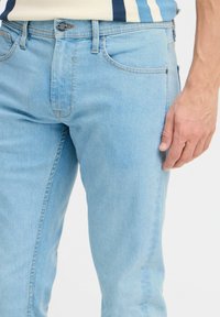 Jeans in denim azzurro chiaro con un design a gamba dritta, cinque tasche e chiusura con bottone, arricchiti da dettagli di cucitura sottili.