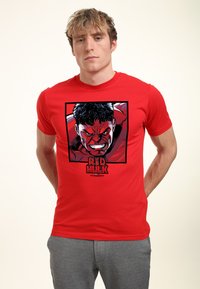 Rød T-shirt med et grafisk tryk af en hård karakter med et vredt udtryk, sorte konturer og teksten "RED HULK" nederst.