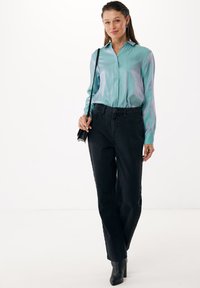 Lichtblauwe satijnen blouse met knopen, gecombineerd met zwarte high-waisted jeans met zijknopen. Zwarte hoge laarzen maken de look af.