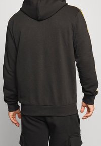 Hoodie i mörkgrått med gula accentränder längs ärmarna, med en avslappnad passform och ribbad mudd och nederkant.