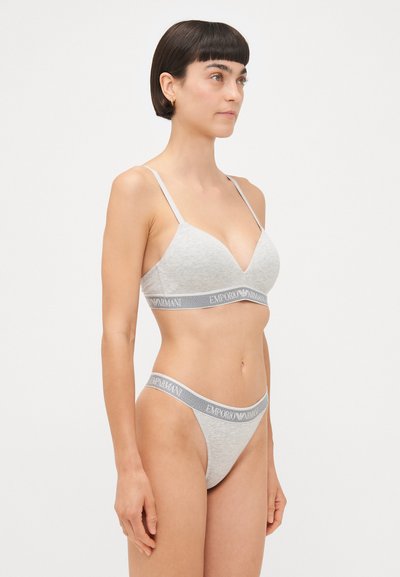 Light grey seamless bra with a plunging neckline and thin adjustable straps, paired with matching thong featuring a branded elastic waistband.