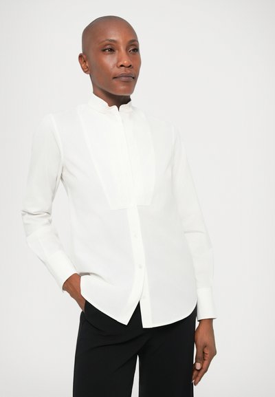Biela košeľa s dlhým rukávom a mandarínkovým golierom, s gombíkovou prednou časťou a detailami s plisovaním. Hladká textúra a prispôsobený strih.