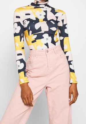 Golf z długim rękawem w żółty, czarny, biały kwiatowy i abstrakcyjny wzór, zestawiony z jasnoróżowymi spodniami z wysokim stanem.