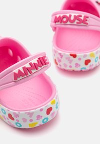 Rosa barneklippsko med "MINNIE" og "MOUSE" skrifttype. Basen har en hvit bakgrunn med fargerike blomster- og hjerte mønstre. Mykt, teksturert materiale.