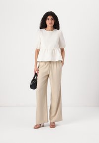Valge peplum-stiilis top, tekstureeritud kangas, puffy varrukad; beežid laiad püksid; väike must käekott; rihmadega pruunid kontsad.