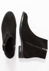Bottines en daim noir avec un bout arrondi, une fermeture éclair latérale et un petit talon bloc. Texture lisse avec des coutures minimales et des accents discrets.