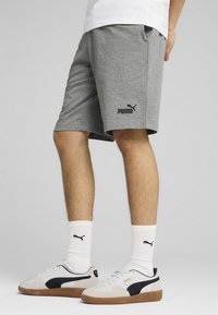 Pelēki sporta šorti ar melnu Puma logo, ceļgala garumā, izgatavoti no mīkstas kokvilnas maisījuma auduma. Apvienoti ar baltiem zeķēm un kedām.