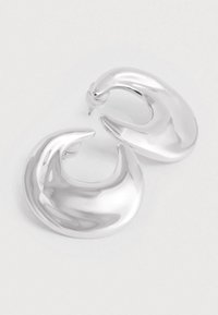 O pereche de cercei hoop în formă de semilună, strălucitori și argintii, cu tăieturi cu spate pe un fundal alb simplu.