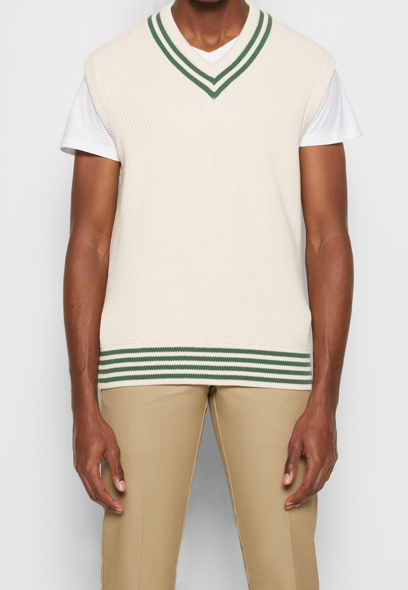 Ärmellose, cremefarbene Strickweste mit tiefem V-Ausschnitt, ausgestattet mit grün gestreiften Akzenten am Ausschnitt und Saum. Strukturiertes Gewebe.