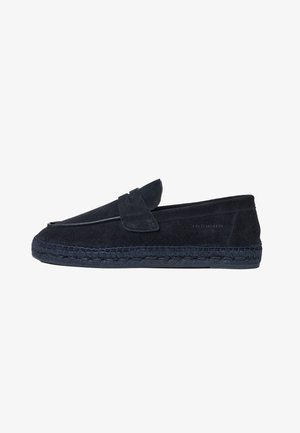 Mørkeblå ruskindsmokasin af slipper-stil har en syet sål og en forreste klap. Designet inkluderer vævede detaljer langs sålen.