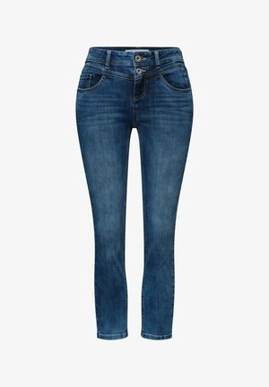 Person iført blå jeans med høj talje og dobbelt knappelukning, hvid skjorte stukket ned i, og pink jakke med guldknapper.