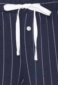 Ναυτικό μπλε παντελόνι με λευκή κορδ�έλα και κλείσιμο με κουμπί. Μαλακό ύφασμα με κάθετες ρίγες και λεπτομέρεια με πλαϊνές τσέπες.