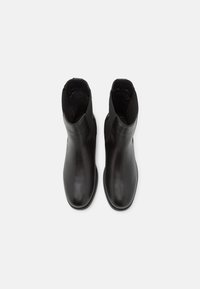 Bottes chelsea en cuir noir avec une finition lisse, des panneaux latéraux élastiques et des bouts ronds, présentant un design minimaliste sans matériel visible.