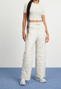 Lekki, pikowany, kremowe spodnie ze ściągaczem w talii, w połączeniu z dopasowanym, krótkim rękawem jasnoszarym topem oraz szarymi sneakersami.