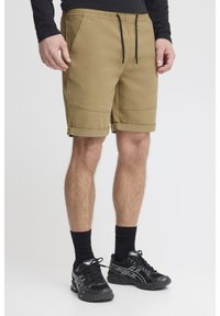 Khaki shorts med elastisk midja och dragsko, med rullade fållar och sidofickor, kombinerade med svarta sportskor och strumpor.