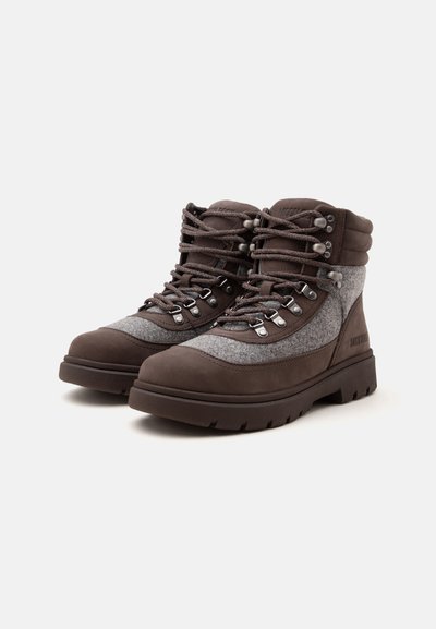 Paire de chaussures de randonnée marron et grises avec semelles épaisses en caoutchouc et œillets métalliques pour lacets, montrée légèrement en angle sur fond blanc.