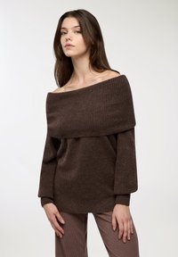 Brązowy sweter bez ramion z przeplatanym detalem, długimi rękawami i miękką teksturą, noszony z w kratkę spodniami.