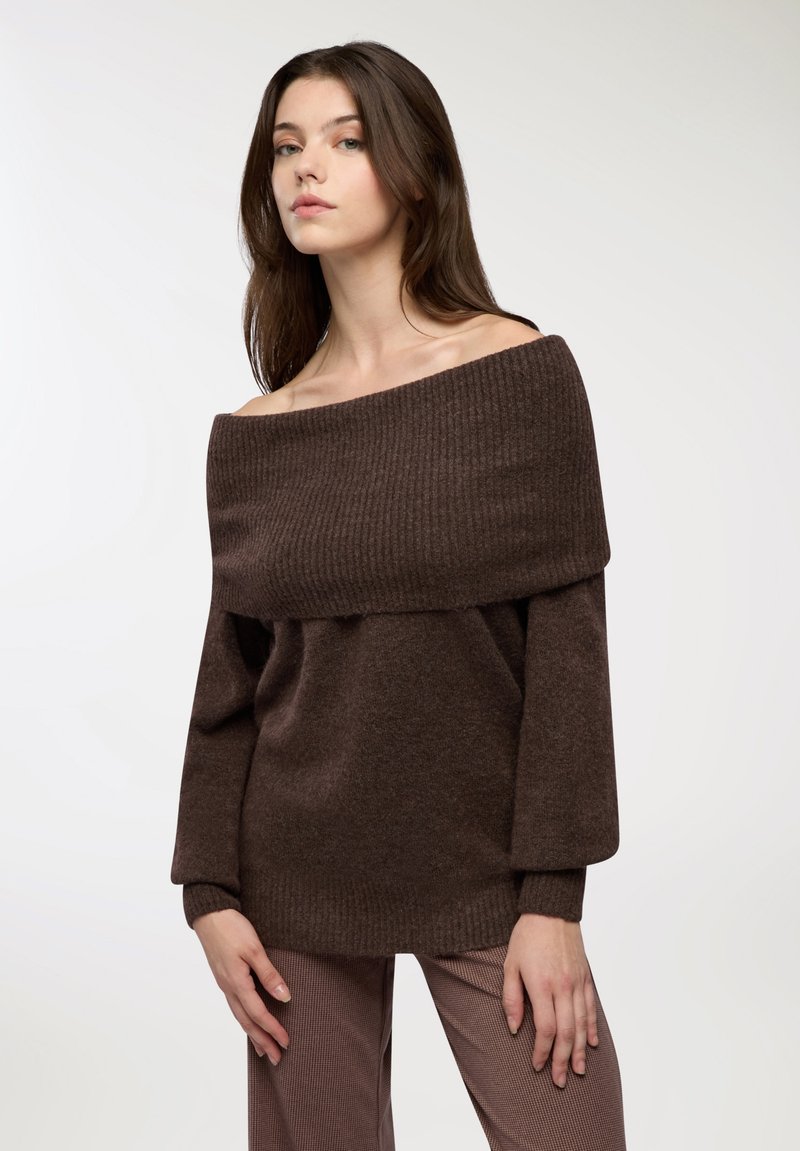 Brązowy sweter bez ramion z przeplatanym detalem, długimi rękawami i miękką teksturą, noszony z w kratkę spodniami.