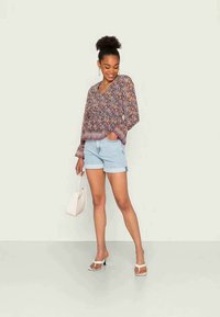 Blusa leve com padrão floral e mangas longas, combinada com calções de ganga azul claro. Acessórios incluem uma pequena bolsa branca e sandálias.