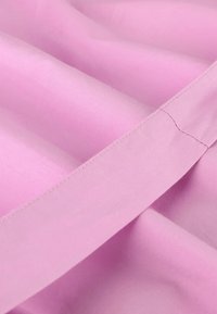 Lys rosa stoff med jevn tekstur, med en pent sydd kant. Materialet ser mykt ut og er litt glinsende.