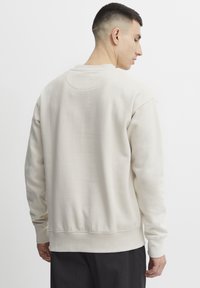 Sudadera de cuello redondo beige hecha de una mezcla de algodón, con puños y dobladillo de canalé, con una textura suave y detalles de costura mínimos.