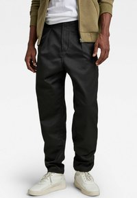 Pantalons noirs, fuselés, en tissu lisse avec poches avant. Associés à des baskets blanches et une veste zippée légère olive.