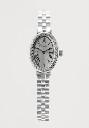 Ασημένιο ρολόι Timex με οβάλ καντράν, ρωμαϊκούς αριθμούς, κρυστάλλινη στεφάνη και συνδεδεμένο μεταλλικό μπρασελέ που δείχνει ώρα 10:10.