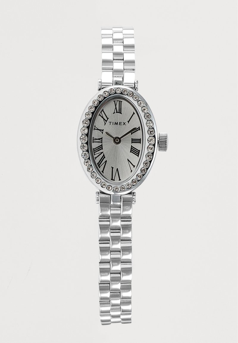 Montre Timex argentée avec cadran ovale, chiffres romains, lunette en cristal et bracelet métallique maillé affichant l'heure 10h10.
