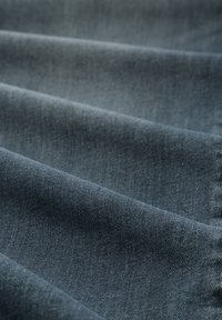 Sötét kék-szürke denim anyag sima felülettel, amelyen finom színeltérések és klasszikus diagonális szövési minta látható.