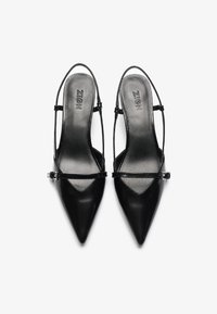 Svarta pumps med spetsig tå och glänsande yta, tunna remmar och ett litet spänne. Designade med en elegant silhuett och mjukt innerfoder.