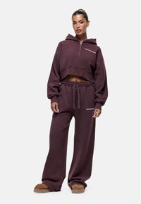 Bordeaux cropped hoodie met rits en tekstdetail, gecombineerd met bijpassende wijde sweatpants. Zachte stof met een relaxte pasvorm.
