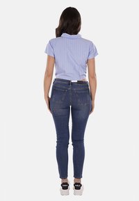Camicia azzurro chiaro a maniche corte con righe bianche verticali, abbinata a jeans scuri aderenti e sneakers bianche con dettagli neri.