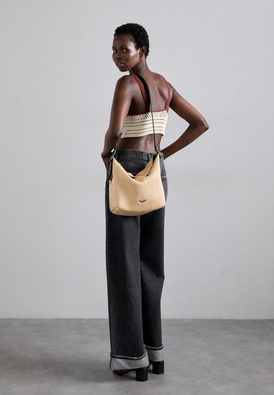 Borsa a tracolla beige intrecciata con una forma morbida, abbinata a jeans scuri a vita alta e a un top in maglia corto con un motivo decorativo.