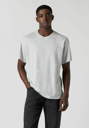 Grå T-shirt i afslappet pasform, lavet af blødt bomuldsstof med korte ærmer og rund halsudskæring, kombineret med mørke jeans.