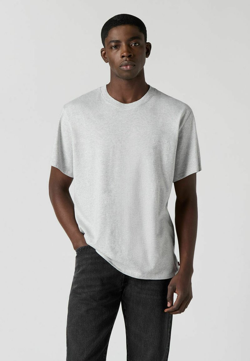 Graues T-Shirt in entspannter Passform, aus weichem Baumwollstoff, mit kurzen Ärmeln und rundem Ausschnitt, kombiniert mit dunklen Jeans.