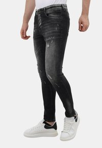 Zwarte distressed skinny jeans met vervaagde delen en scheuren, gecombineerd met witte sneakers met een zwart accent op de hiel.