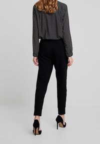 Joggers negros ajustados con puños elásticos combinados con una blusa de lunares. Zapatos de tacón añaden una textura y un color contrastantes.