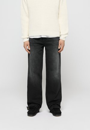 Zwarte wijde spijkerbroek van denim, met een vervaagde afwerking. Gecombineerd met een textuurcreme trui, die over een gestreept shirt is gedragen.