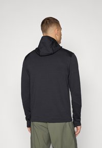 Felpa nera con tessuto testurizzato, design aderente e collo alto. Maniche lunghe con aperture per pollici, abbinata a pantaloni corti verde oliva chiaro.