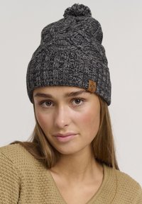 Beanie grigio lavorato a maglia con un motivo testurizzato, dotato di un pompon in cima e di un piccolo tag logo marrone sul lato.