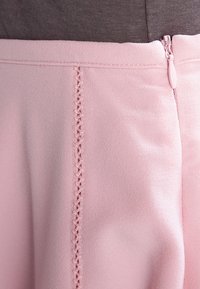 Falda de color rosa claro hecha de tela suave, que cuenta con un cierre de cremallera lateral y costuras decorativas a lo largo de las juntas. Diseño sencillo sin patrones.