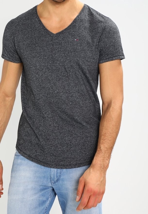 Grau V-Ausschnitt T-Shirt aus weichem Stoff mit kurzen Ärmeln und kleinem Logo auf der linken Brust, kombiniert mit hellblauen Jeans.