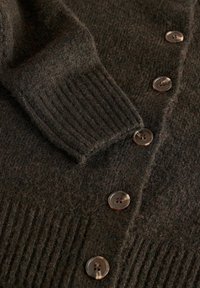 Dark brown knitted cardigan with ribbed cuffs and hem, featuring four marbled brown buttons down the front.