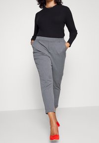 Pantalons gris ajustés avec une taille plate et des poches latérales, associés à un haut noir à manches longues à côtes et des escarpins rouges à bout pointu.