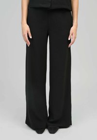 Pantalon noir à jambe large en tissu lisse, doté d'une taille haute, de lignes épurées et de plis subtils pour une structure ajoutée.