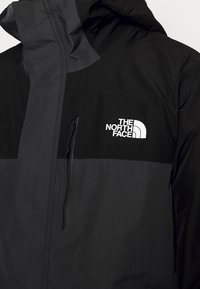 Veste noire et gris foncé avec une poche zippée à l'avant et le logo "The North Face" sur le côté gauche de la poitrine, dotée d'une capuche.