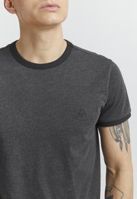 Czarny t-shirt w ciemnoszarym kolorze z czarnym prążkowanym kołnierzykiem i rękawami, z małym wytłoczonym logo na piersi. Miękka, teksturowana tkanina.