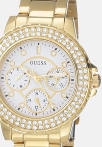 Kulta sävyinen kello, jossa on kristallikoristeinen kehys, valkoinen kellotaulu, kolme alataulua ja linkkiranneke. Ominaisuuksina ovat rohkeat mustat tuntimerkit ja viisarit.